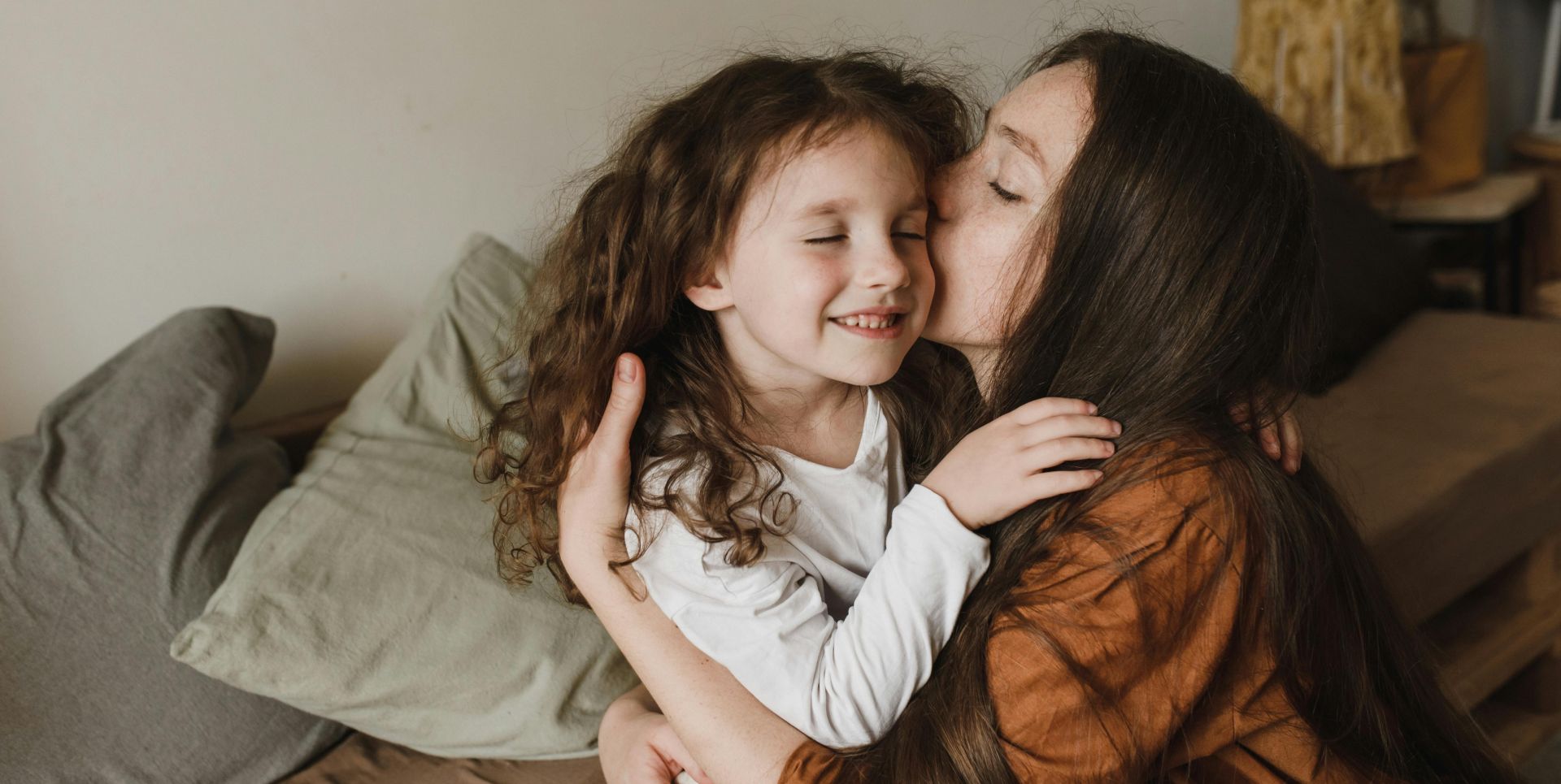 A touching moment of a mother kissing her daughter indoors, radiating love and warmth.