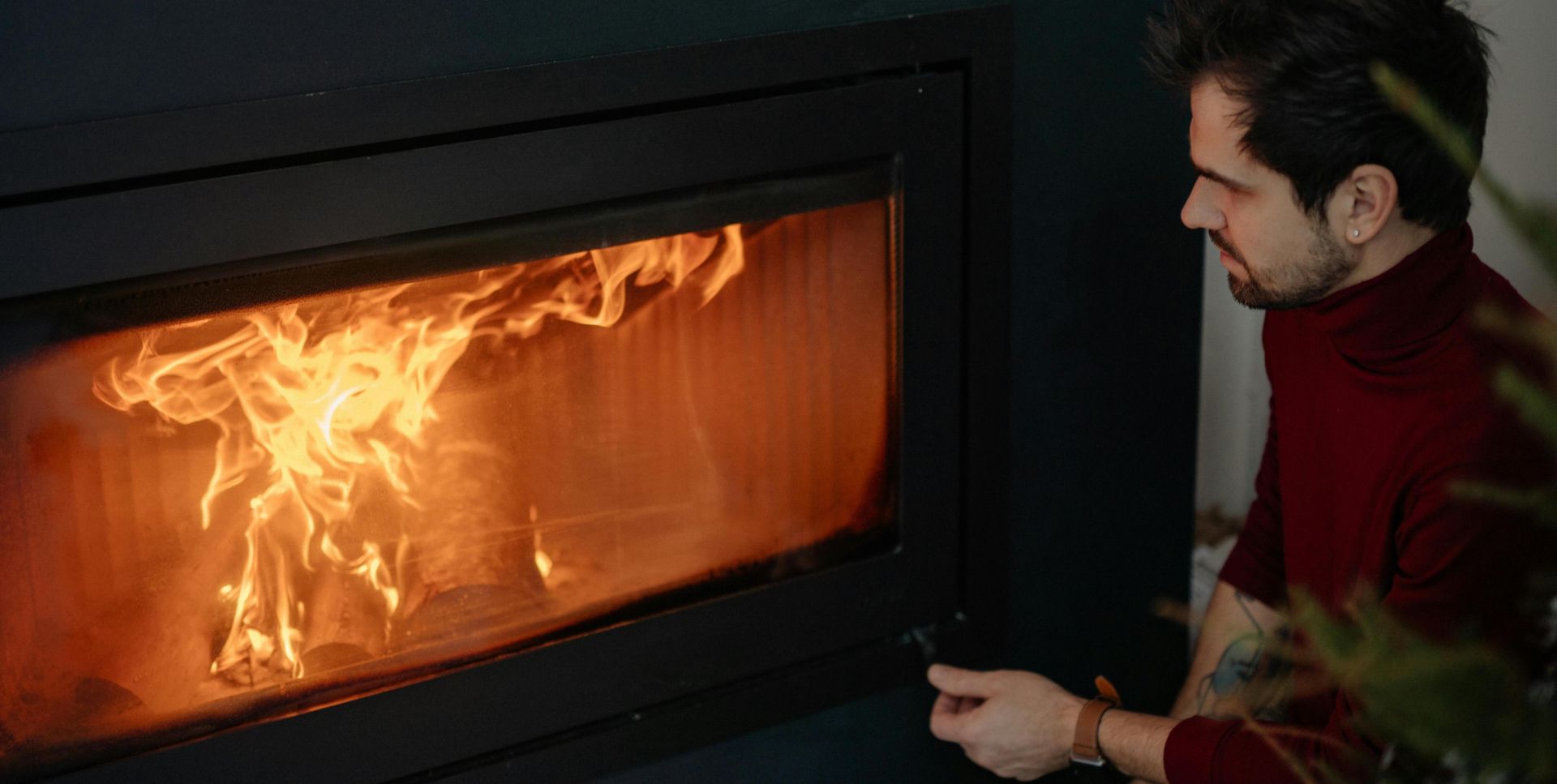 Man in cozy red sweater enjoying warmth from modern fireplace indoors.